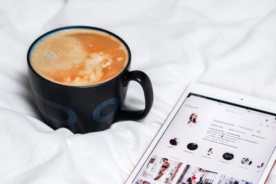 Tablet mit Instagram auf Bettdecke neben Kaffee